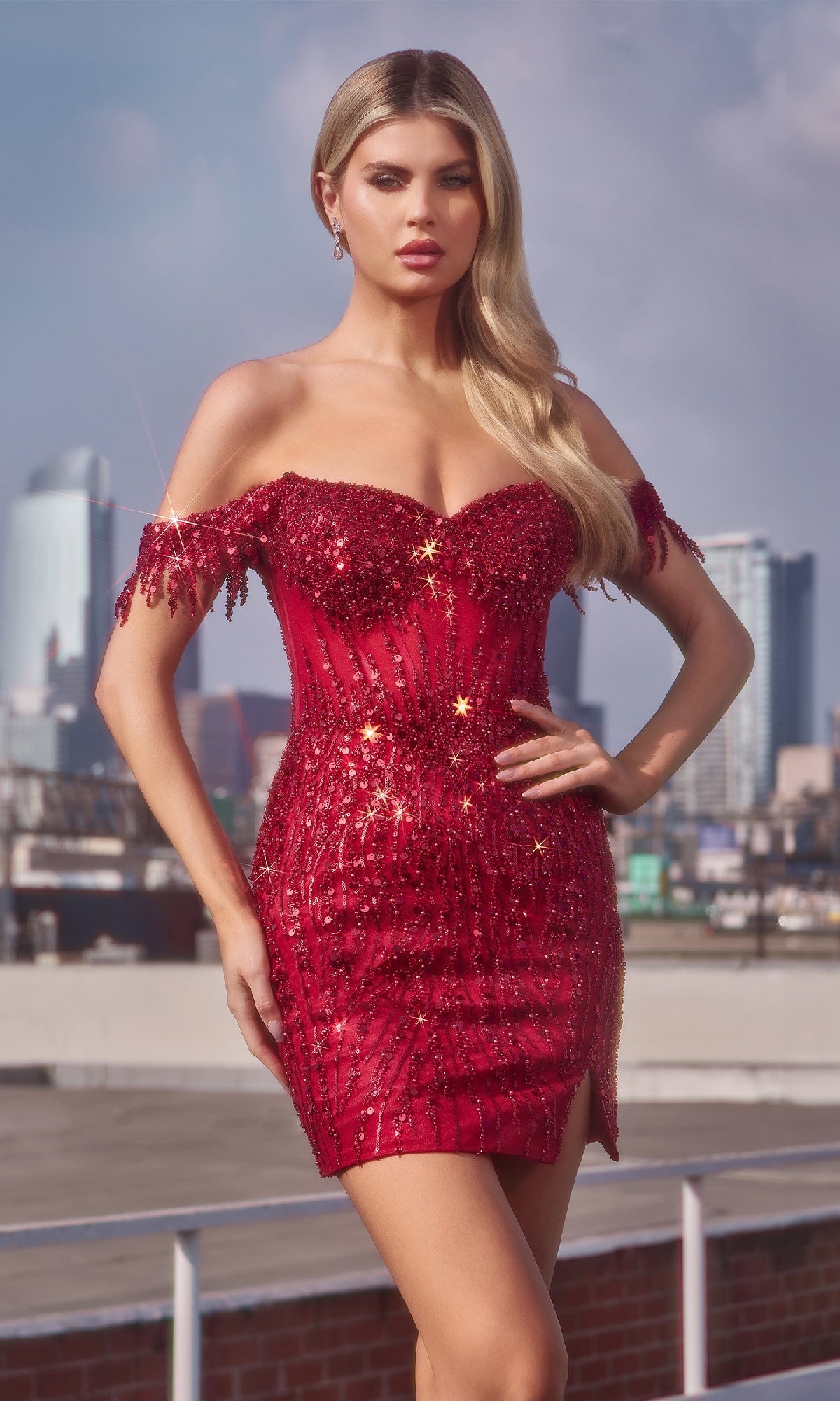 A woman stands outdoors before a city backdrop, wearing the Off-Shoulder Short Sequin Prom Dress: Ladivine CC461, featuring sparkling sequins and beaded accents, with her hair in loose waves.